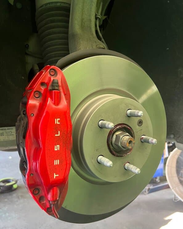 A red Tesla brake caliper on a rotor, with the wheel removed