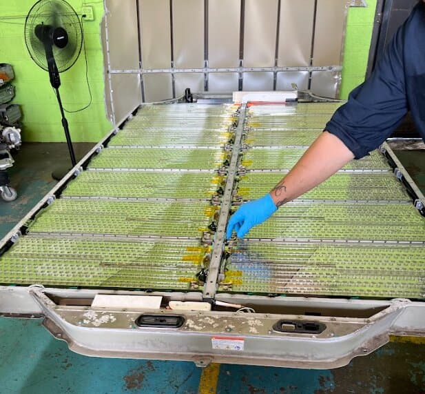 A technician working on an opened Tesla high-voltage battery pack